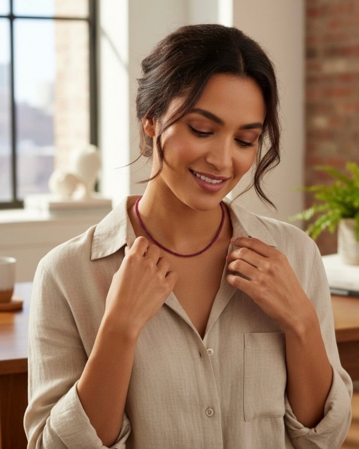 Amelia Jane Handmade Creations faceted ruby necklace worn by a woman in a beige linen shirt in a bright home office.