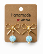 Amelia Jane Handmade Creations gold plated bow stud earrings with dangling light blue marbled beads on display card