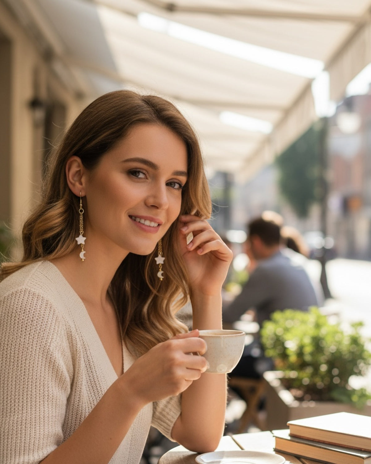 Amelia Jane Handmade Creations celestial dangle earrings with mother of pearl stars on a woman at an outdoor cafe