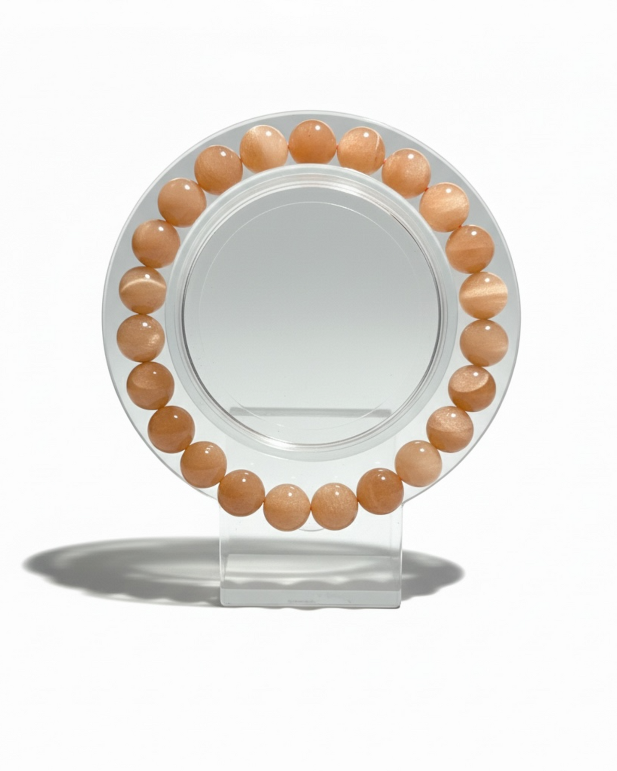 Amelia Jane Handmade Creations 7-inch peach moonstone beaded bracelet on a clear circular display stand.